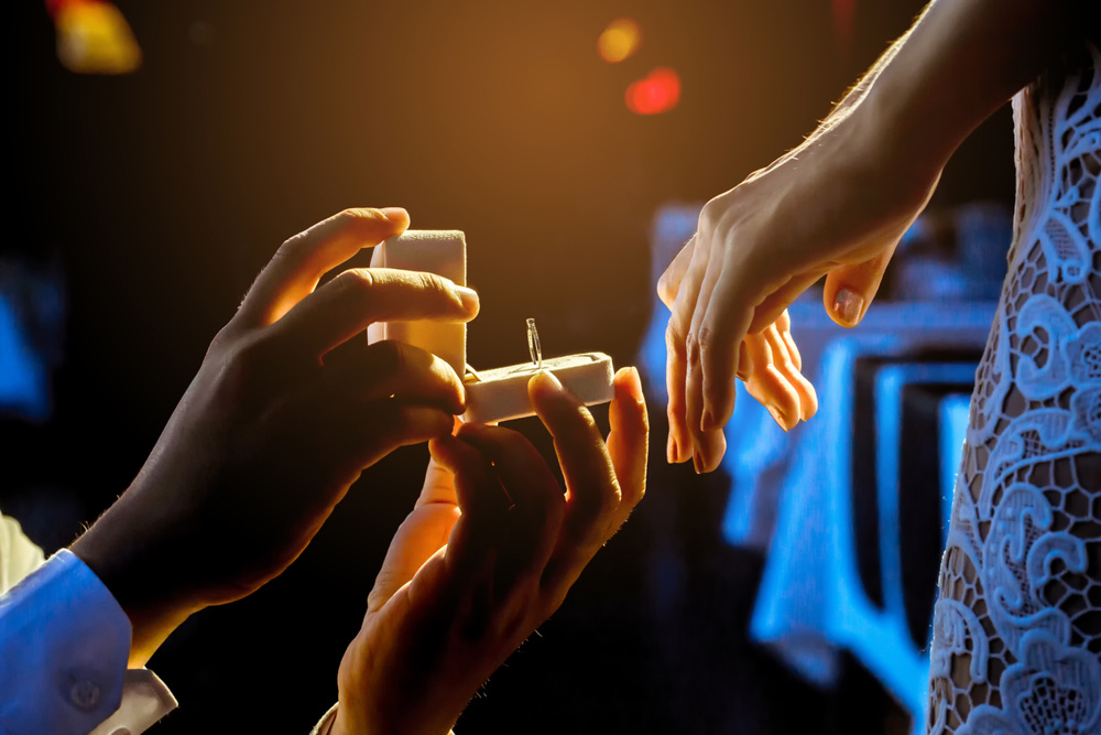 Man proposing to his girlfriend with a ring in a dimly-lit restaurant