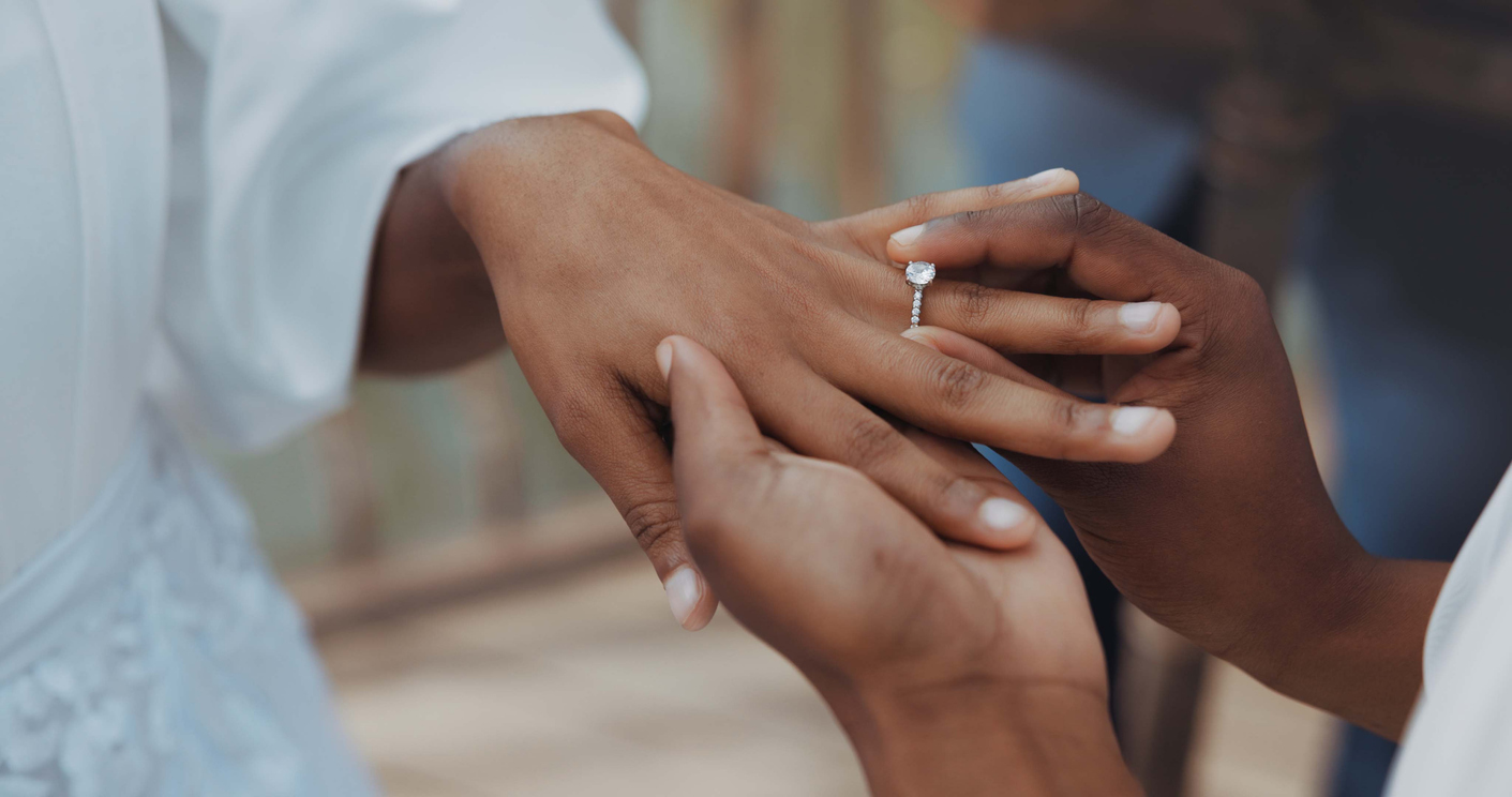 a couple holding hands, putting on engagement ring