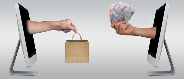 Two hands emerge from the blacked-out screen of a computer, holding a paper bag and money